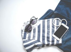 Flat lay image featuring sunglasses, striped top, jeans, and smartphone, ideal for fashion and lifestyle themes.